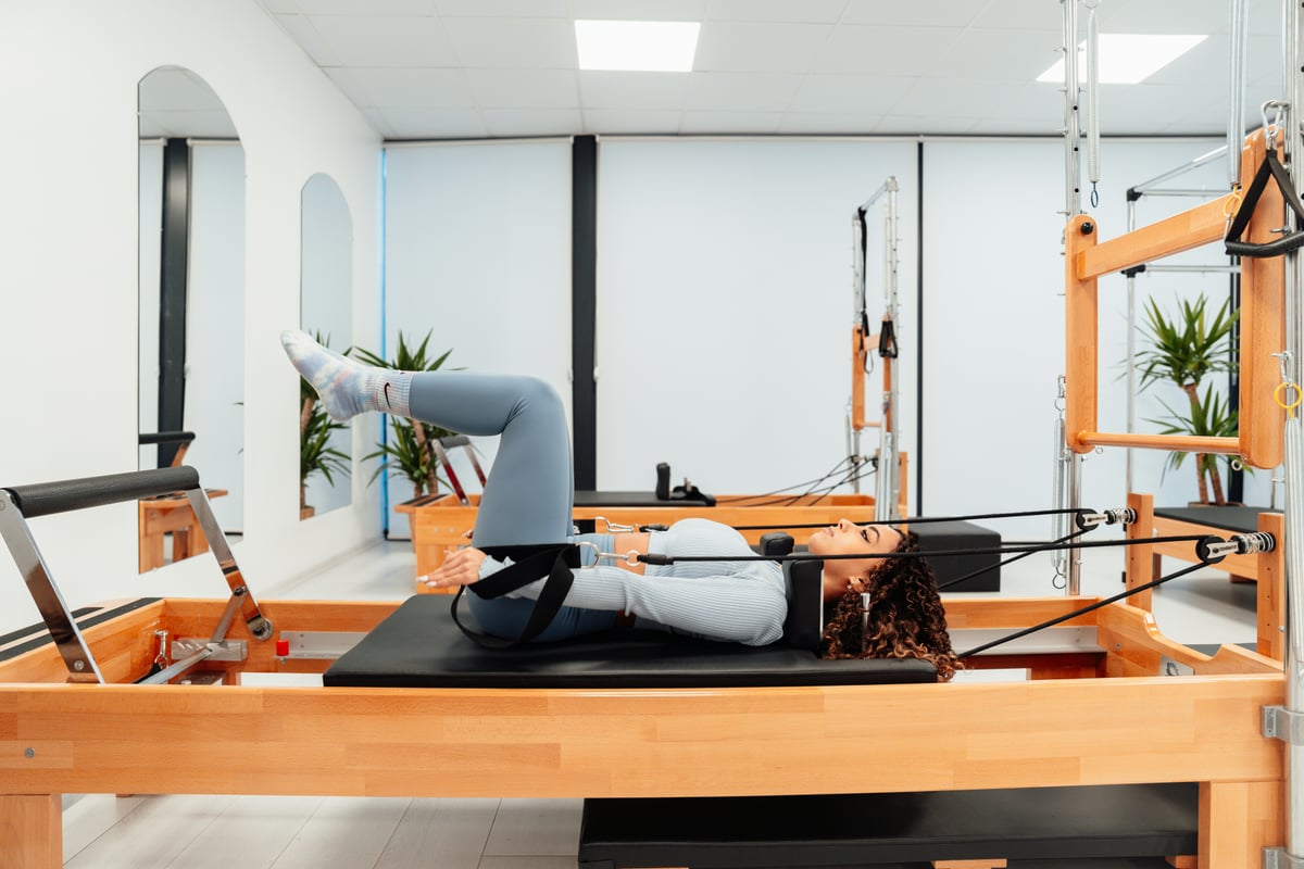 Aluna praticando Pilates no reformer com instrutora em estúdio iluminado